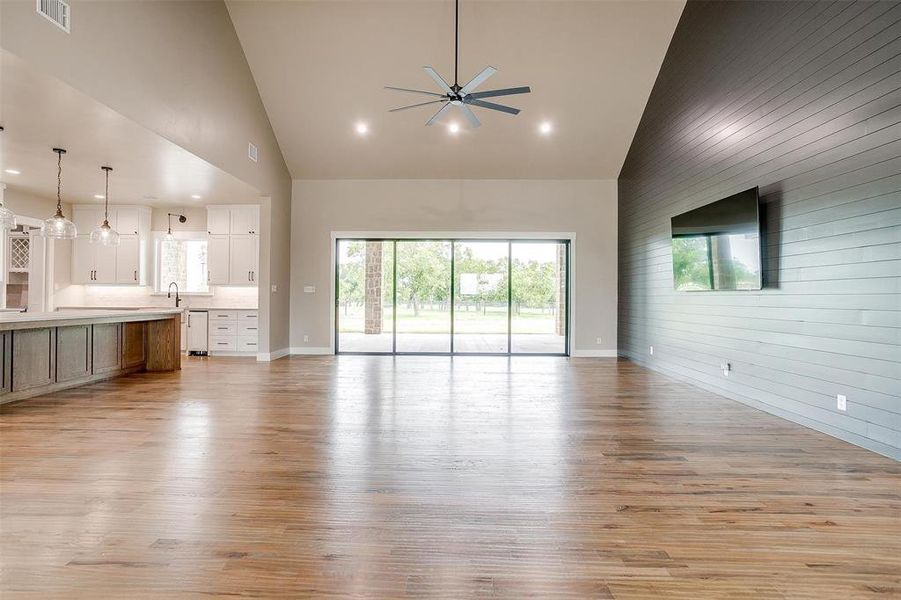 Unfurnished living room featuring high vaulted ceiling, a ceiling fan, light wood-type flooring, a sink, and wooden walls Unfurnished living room featuring high vaulted ceiling, a ceiling fan, light wood-type flooring, a sink, and wooden walls
