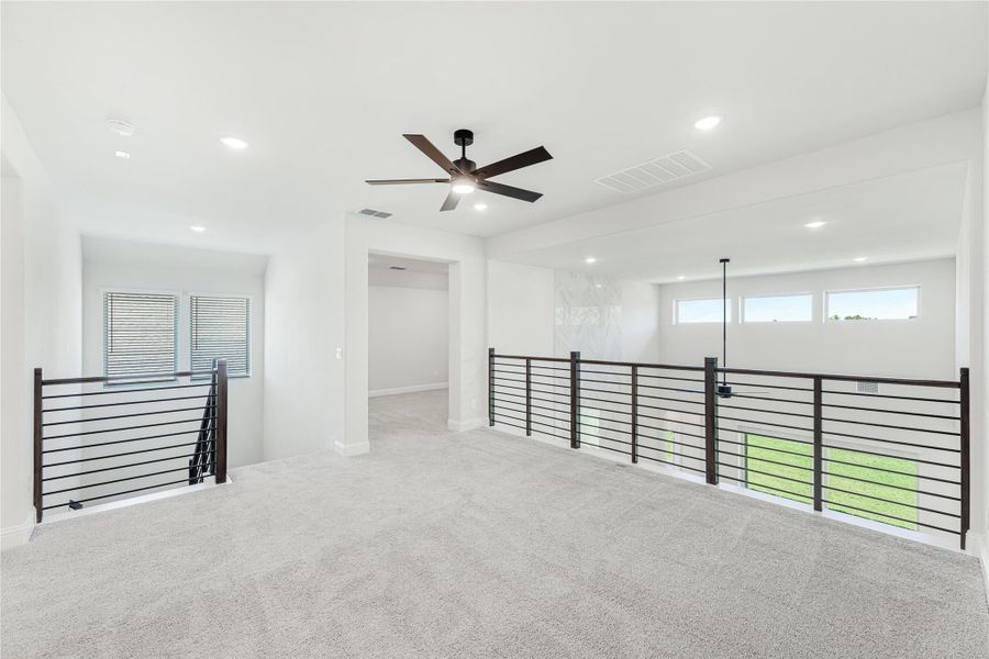 Open upstairs loft with carpet, ceiling fan, and dark metal railing overlooking lower level