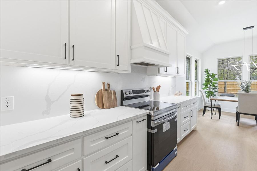 Kitchen with stainless steel electric stove, white cabinets, light stone counters, light wood-type flooring, and hanging light fixtures