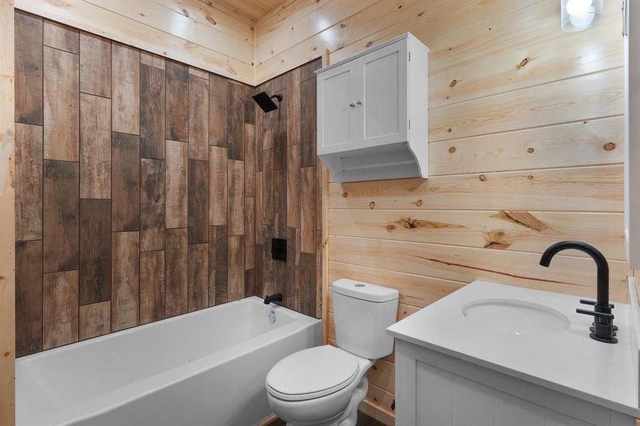 Bathroom featuring wood walls, toilet, vanity, and shower / tub combination Bathroom featuring wood walls, toilet, vanity, and shower / tub combination