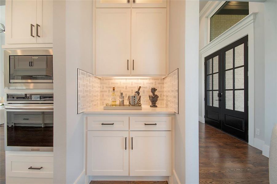 Bar featuring appliances with stainless steel finishes, white cabinetry, decorative backsplash, dark wood-type flooring, and french doors Bar featuring appliances with stainless steel finishes, white cabinetry, decorative backsplash, dark wood-type flooring, and french doors