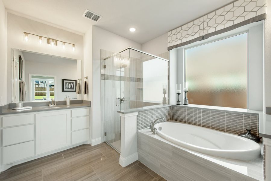 Master bathroom with soaking tub, glass walk-in shower, double vanity, and gray tile accents