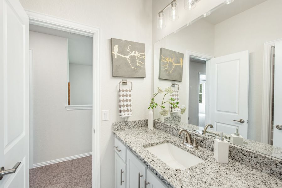 Bathroom vanity with granite countertop, white cabinets, undermount sink, and large mirror with walk-in closet nearby