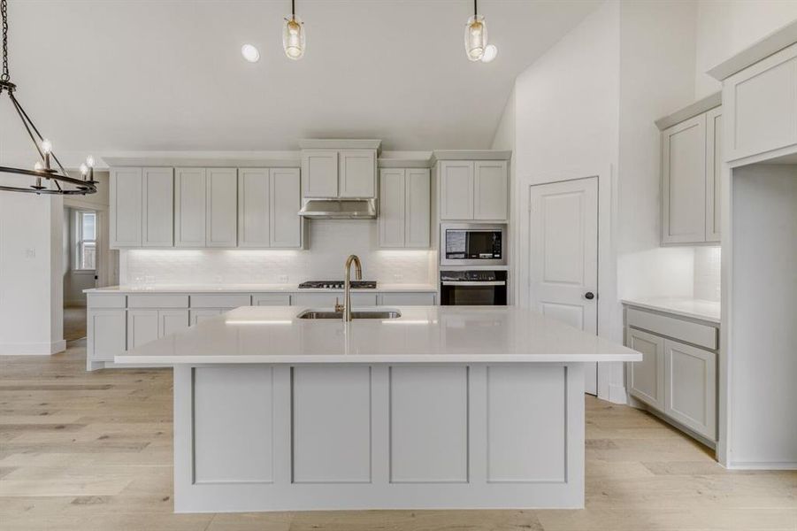 Kitchen with an island with sink, stainless steel appliances, light wood-style flooring, a chandelier, and white cabinets Kitchen with an island with sink, stainless steel appliances, light wood-style flooring, a chandelier, and white cabinets