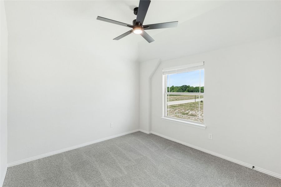 Empty bedroom with vaulted ceiling, ceiling fan, gray carpet, and single window with outdoor view