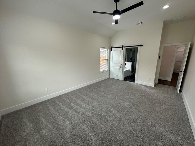 Unfurnished bedroom with carpet floors, lofted ceiling, a barn door, and ceiling fan