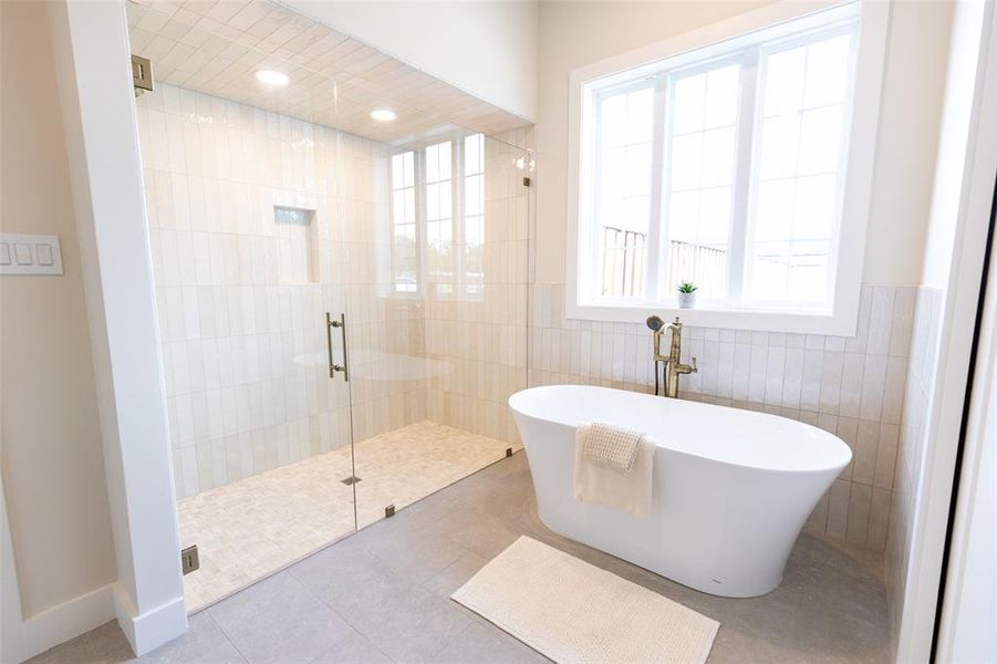 Contemporary bathroom featuring a freestanding soaking tub with a gold-finish floor-mounted faucet, a spacious glass-enclosed shower with subway tile walls and pebble tile flooring, and a large window with white trim