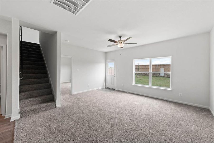 Unfurnished living room featuring stairs, ceiling fan, and carpet floors Unfurnished living room featuring stairs, ceiling fan, and carpet floors