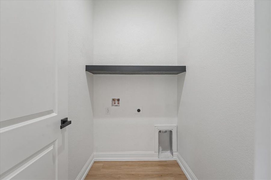 Dedicated laundry alcove featuring a dark wood-finish shelf, light wood-finish flooring, and white baseboards