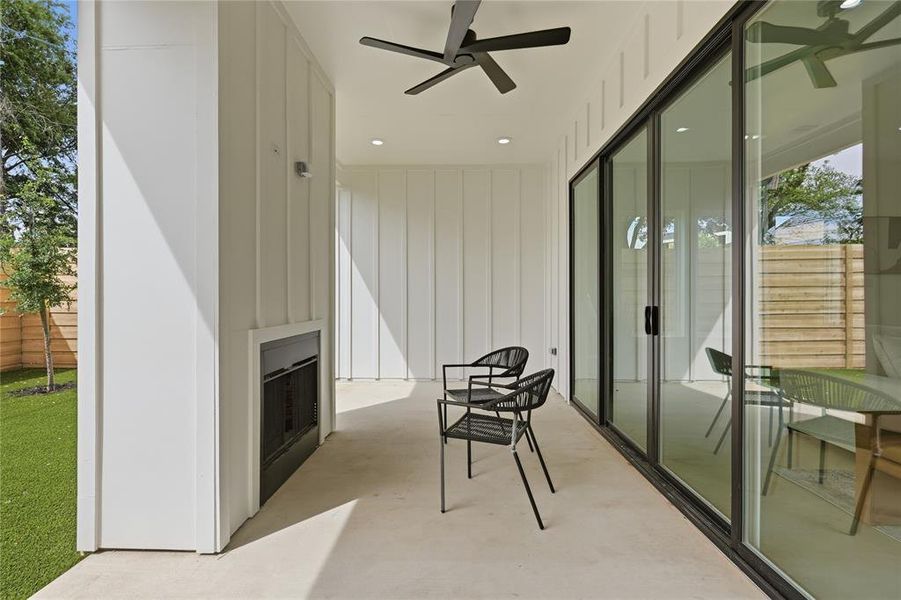 Covered patio featuring a built-in fireplace, board and batten siding, ceiling fan, and recessed lighting