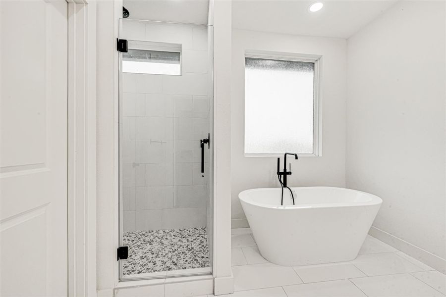 The primary en-suite showcases a stunning standalone soaking tub, a separate glass-enclosed walk-in shower with designer tile and an abundance of natural light.