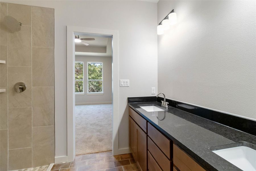 Bathroom featuring double vanity, a tile shower, and a ceiling fan
