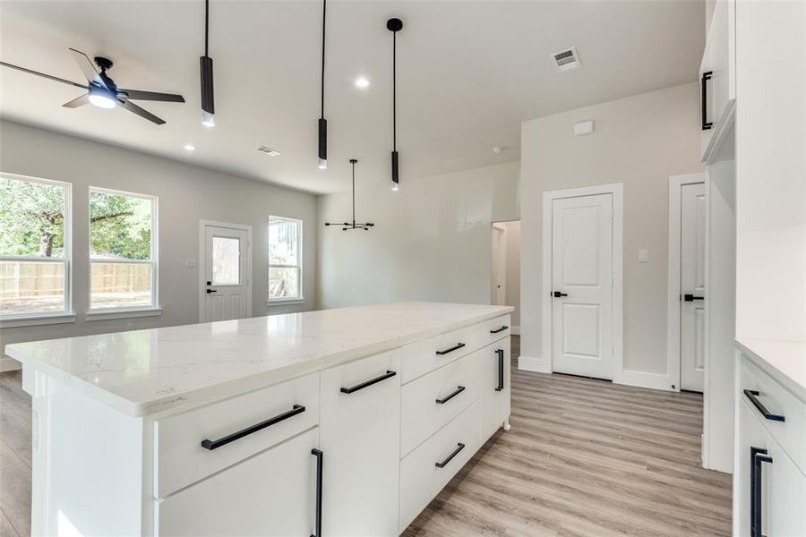 Kitchen with light stone counters, light hardwood / wood-style floors, hanging light fixtures, white cabinetry, and a center island