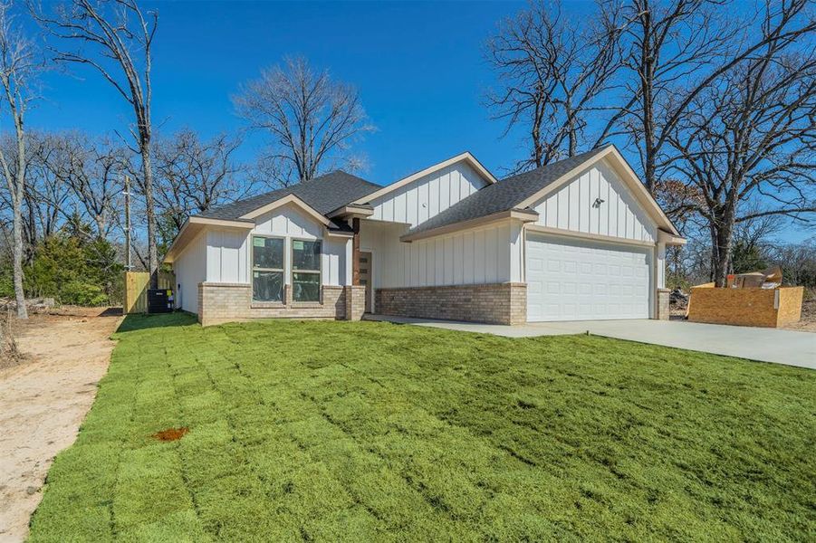 View of front facade with a garage, driveway, a front lawn, board and batten siding, and brick siding