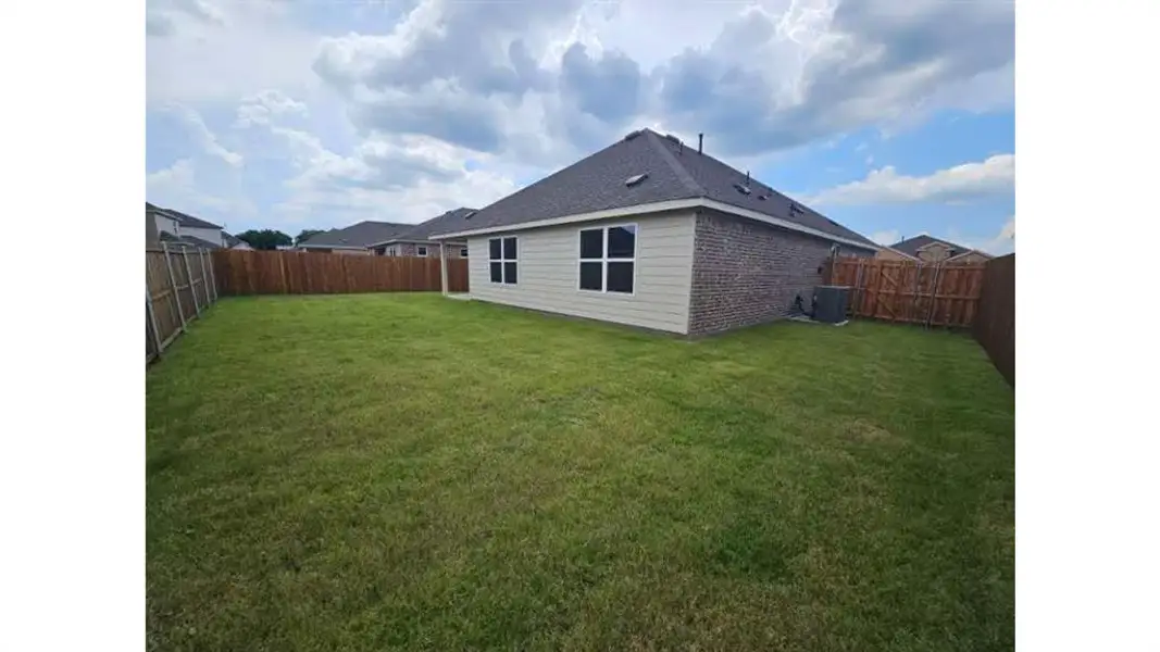 Expansive backyard featuring a large green lawn, full privacy fencing, and a brick and siding exterior