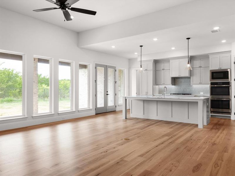 Kitchen with french doors, light wood-type flooring, a breakfast bar, an island with sink, and decorative backsplash