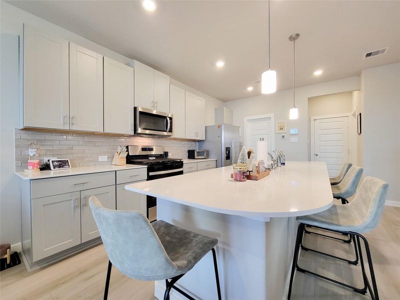 Modern kitchen with sleek white cabinetry and a stylish subway tile backsplash. It features stainless steel appliances, a spacious island with seating, and pendant lighting for a contemporary feel.