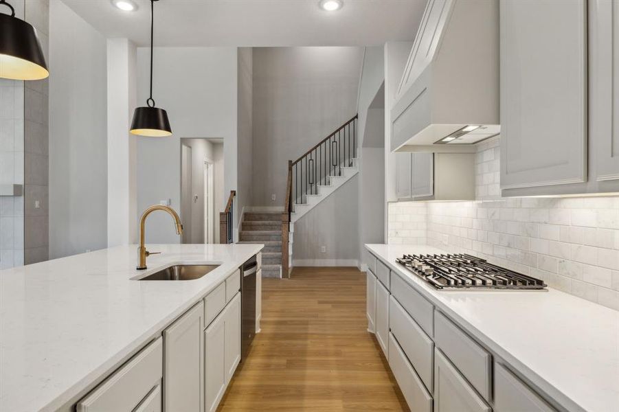 Kitchen with appliances with stainless steel finishes, custom range hood, light wood-style flooring, hanging light fixtures, and white cabinets