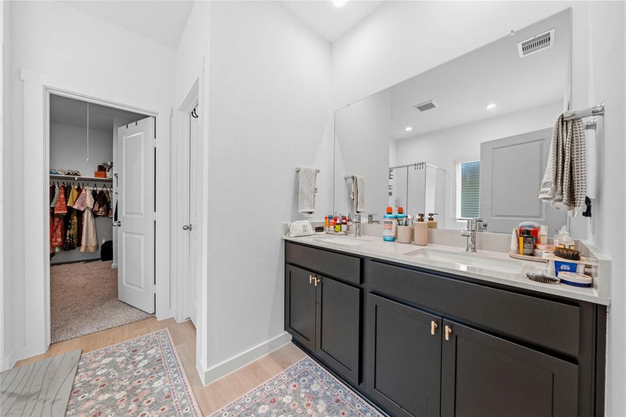 A light-filled primary bathroom showcases a dual vanity, sleek modern finishes, and a large statement mirror, with direct access to a generously sized walk-in closet. A light-filled primary bathroom showcases a dual vanity, sleek modern finishes, and a large statement mirror, with direct access to a generously sized walk-in closet.