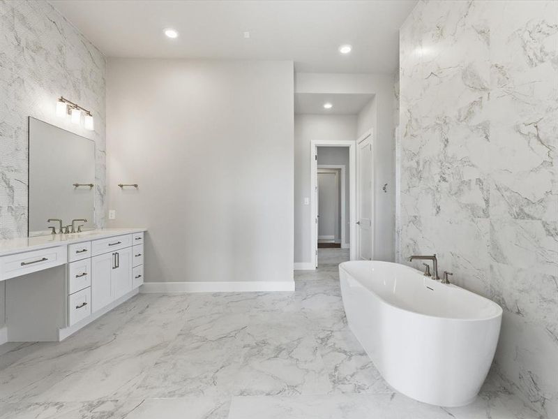 Full bath featuring vanity, a freestanding tub, tile walls, light marble finish flooring, and recessed lighting