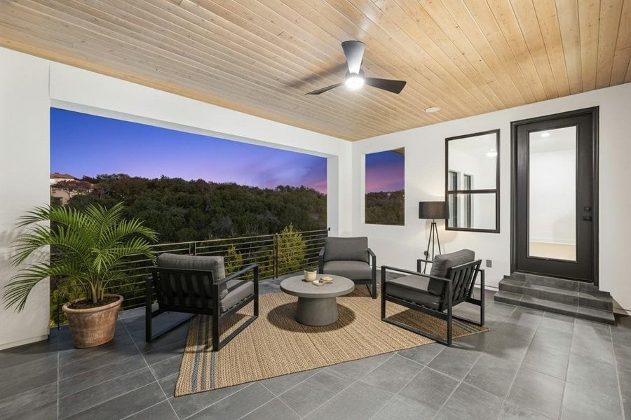 Covered outdoor patio featuring a slatted wood ceiling with a ceiling fan, dark tile flooring, and a modern metal railing