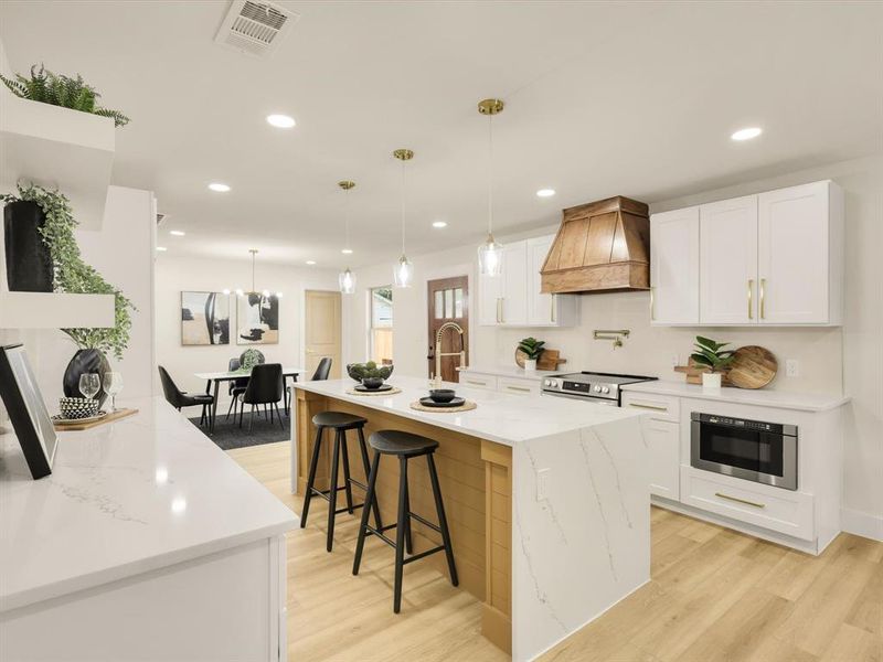 Kitchen with white cabinets, light wood-type flooring, appliances with stainless steel finishes, premium range hood, and pendant lighting