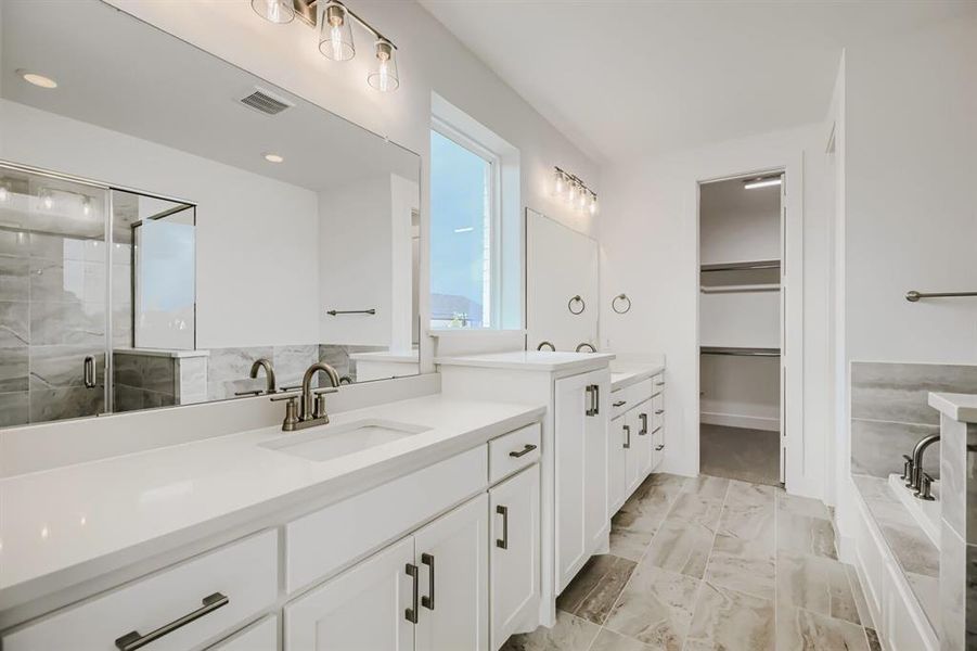 Full bathroom featuring two vanities, a garden tub, a walk in closet, a stall shower, and light marble finish flooring
