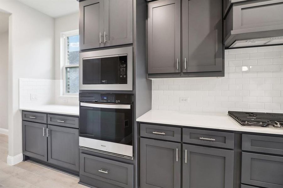 Kitchen featuring decorative backsplash, appliances with stainless steel finishes, gray cabinetry, and range hood