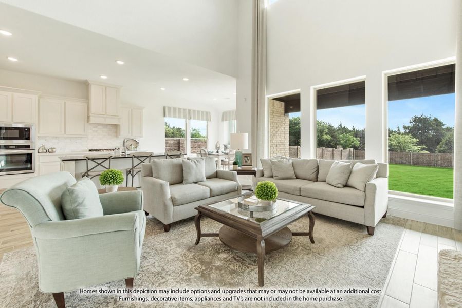 Open-concept living room with high ceilings, gray sofas, and large windows overlooking a backyard, with kitchen visible in background.