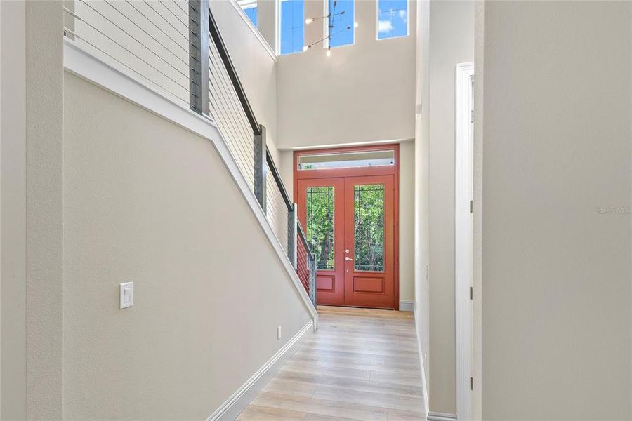 Step into a grand and dramatic foyer that makes an immediate impression with its soaring two-story ceilings and abundant natural light. The impressive double front doors with decorative glass panels create a striking entrance, while a modern staircase with sleek cable railings adds a contemporary touch. This bright and welcoming entryway sets the tone for the quality and design found throughout the rest of the home.
