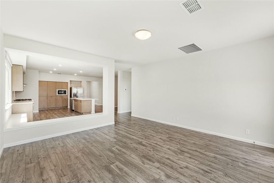 Open living area with wood-look floors and kitchen visible through pass-through opening with wood cabinets and island