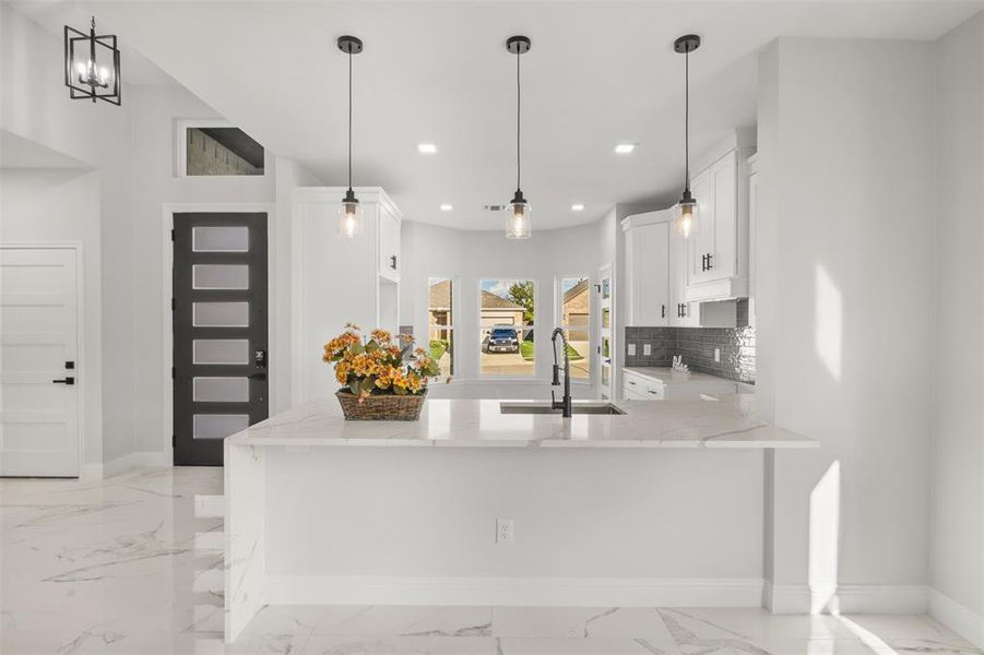 Kitchen with light stone counters, light marble finish flooring, white cabinetry, decorative backsplash, and hanging light fixtures