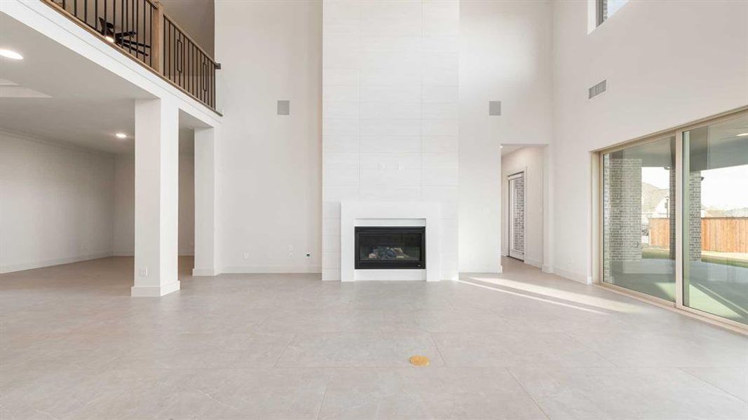 Unfurnished living room with a tiled fireplace, light tile patterned floors, and a high ceiling