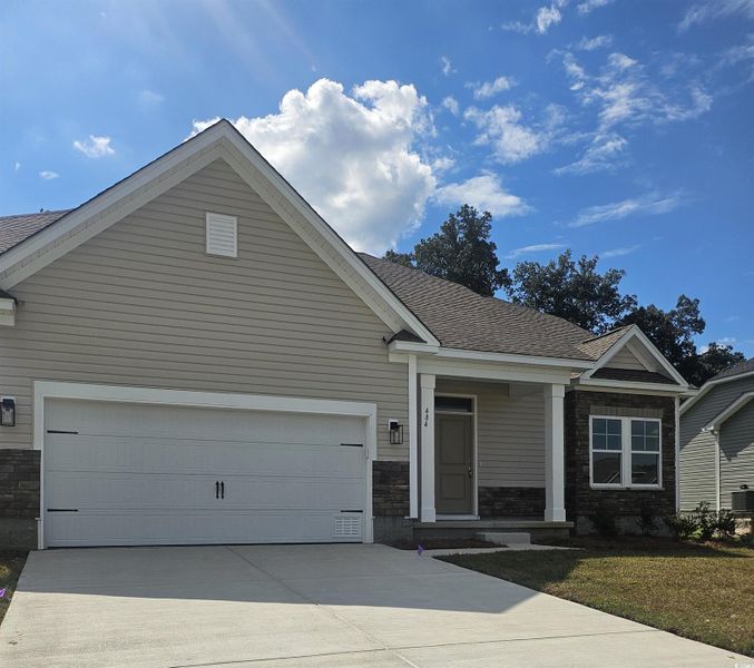 View of front facade featuring stone siding, concrete driveway, covered porch, and a shingled roof
