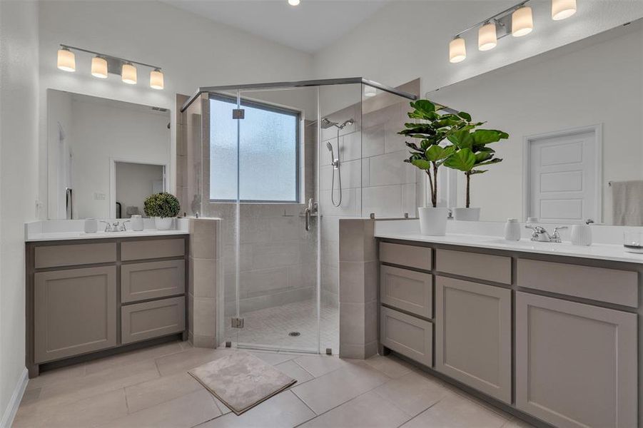 Spacious bathroom featuring a glass-enclosed shower with a frosted window, dual vanity countertops, contemporary gray cabinetry, and tile flooring Spacious bathroom featuring a glass-enclosed shower with a frosted window, dual vanity countertops, contemporary gray cabinetry, and tile flooring