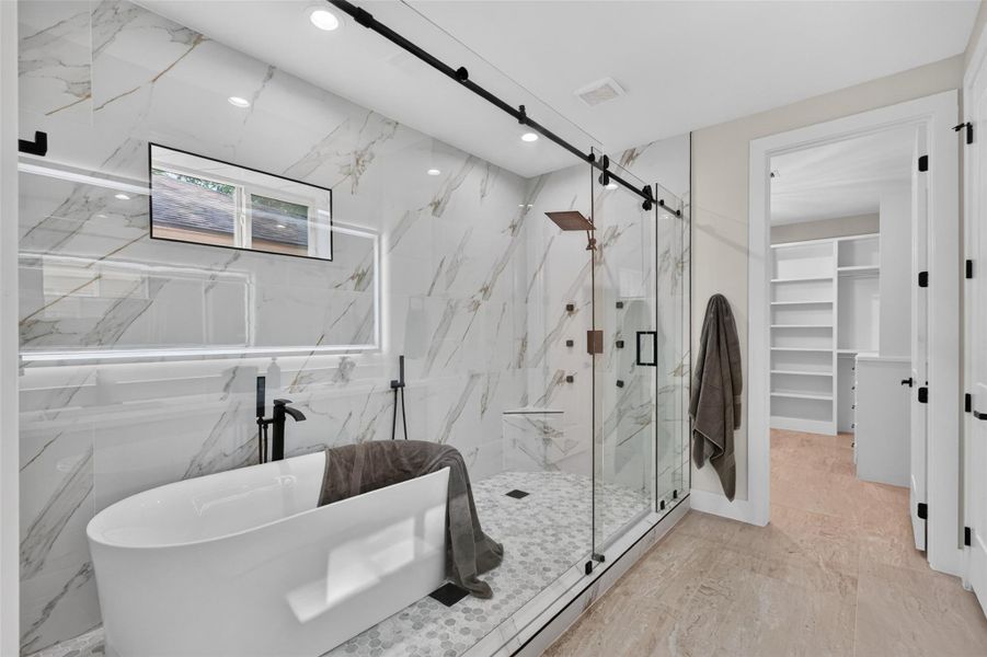 Luxurious bathroom featuring a freestanding tub, spacious glass-enclosed shower, and elegant marble accents, seamlessly connected to a walk-in closet.