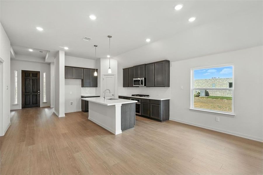 Kitchen featuring recessed lighting, a kitchen bar, decorative light fixtures, light wood-type flooring, and a center island with sink Kitchen featuring recessed lighting, a kitchen bar, decorative light fixtures, light wood-type flooring, and a center island with sink