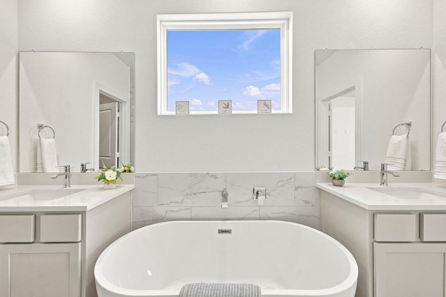 Spa-inspired primary bathroom featuring a freestanding soaking tub, separate vanities with quartz countertops, modern fixtures and abundant natural light. Spa-inspired primary bathroom featuring a freestanding soaking tub, separate vanities with quartz countertops, modern fixtures and abundant natural light.