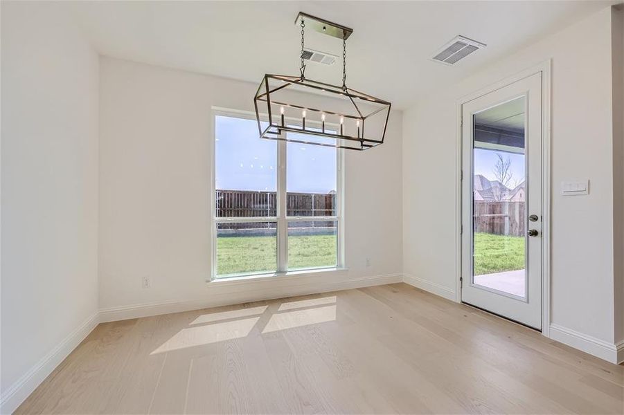 Empty room with a healthy amount of sunlight, light hardwood / wood-style flooring, and an inviting chandelier