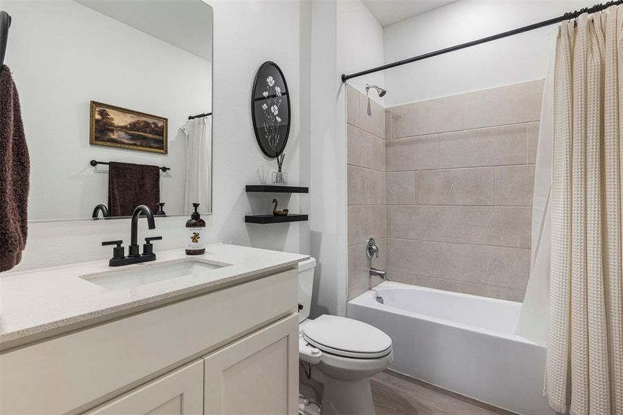 Bathroom featuring a white vanity with a light-toned countertop, black faucet, large mirror, and a bathtub with light-colored subway tile surround Bathroom featuring a white vanity with a light-toned countertop, black faucet, large mirror, and a bathtub with light-colored subway tile surround