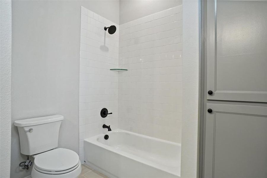 Bathroom with toilet, tile patterned floors, and tiled shower / bath