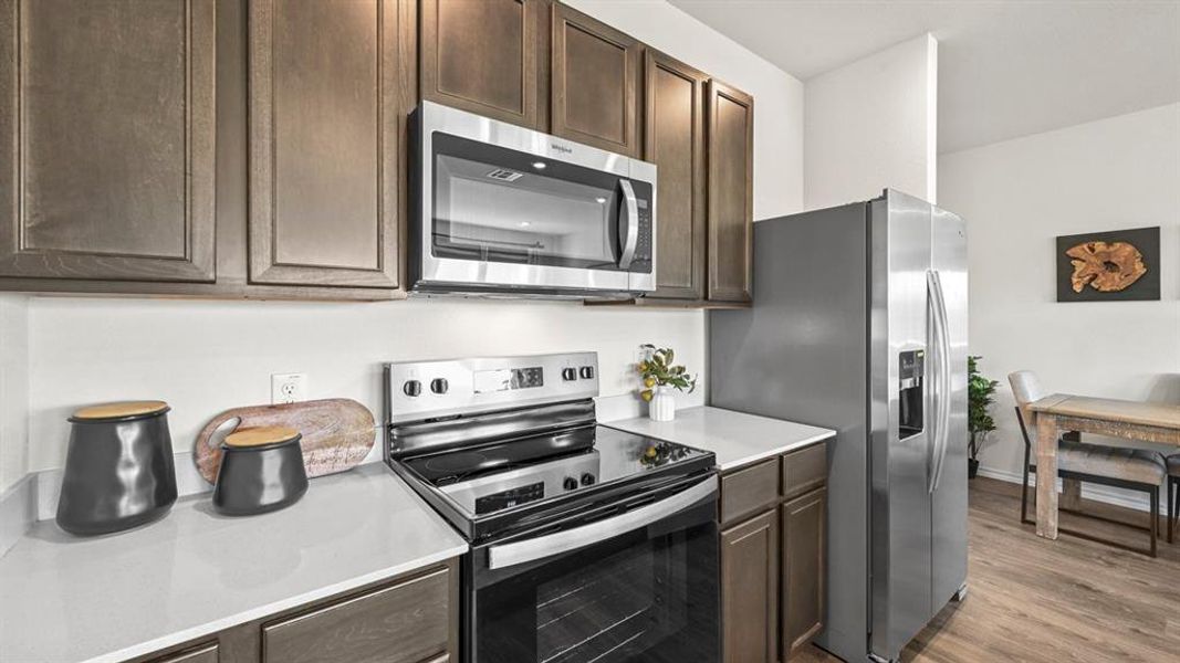 Kitchen with appliances with stainless steel finishes, dark brown cabinetry, light countertops, and light wood-type flooring
