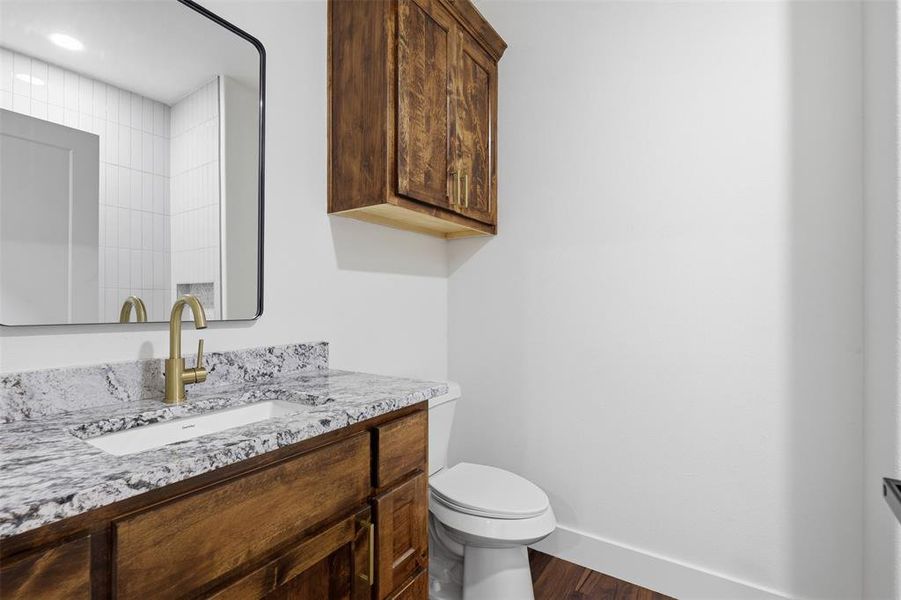 Powder room featuring a wood-finish vanity with granite countertop, undermount sink, and brass-finish faucet Powder room featuring a wood-finish vanity with granite countertop, undermount sink, and brass-finish faucet