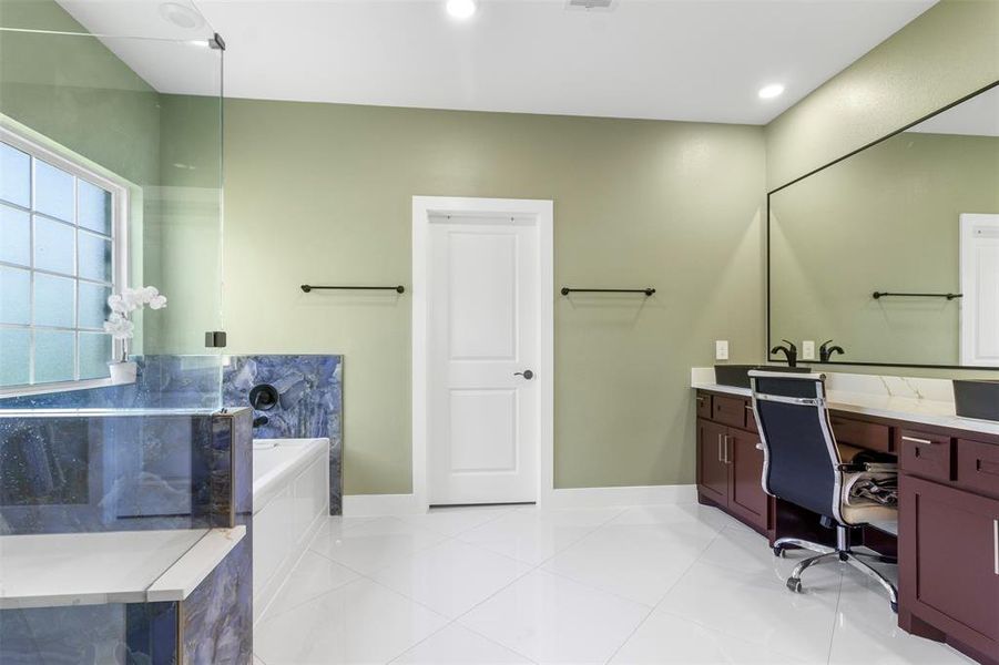 This modern bathroom features a spacious layout with a large vanity and seating area, elegant green walls, and a luxurious bathtub enclosed in glass. Natural light floods in through the frosted window, highlighting the sleek design and ample storage.