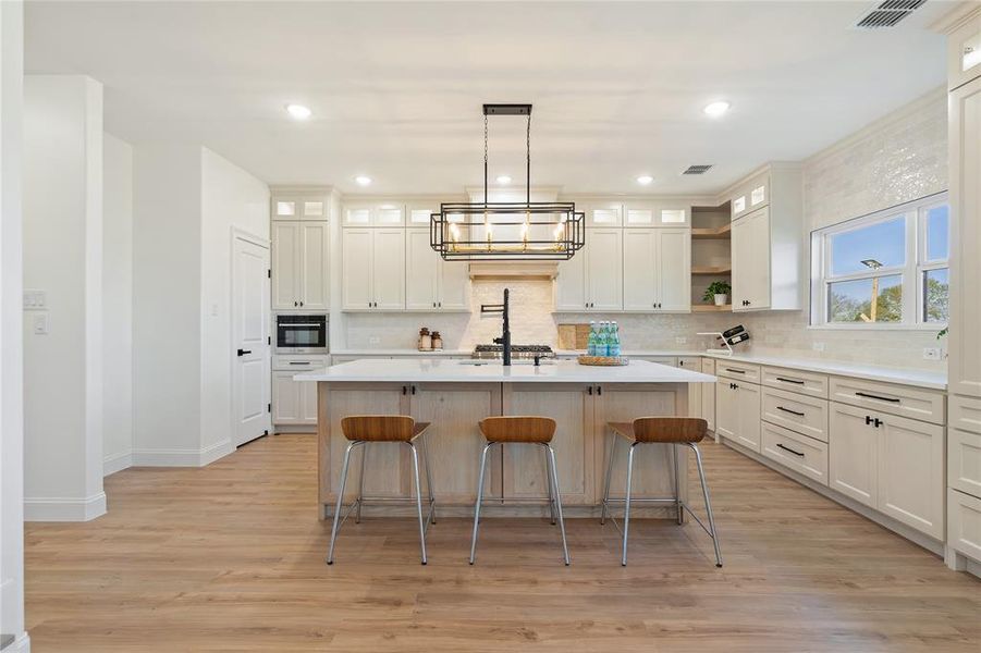 Kitchen featuring appliances with stainless steel finishes, pendant lighting, white cabinets, light hardwood / wood-style floors, and an island with sink