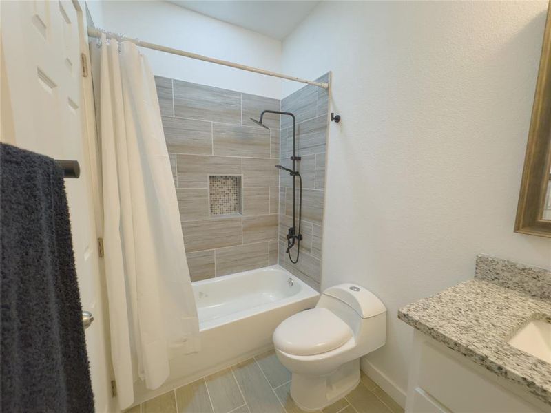 Full bathroom with tile floors, toilet, shower / bath combo with shower curtain, and vanity