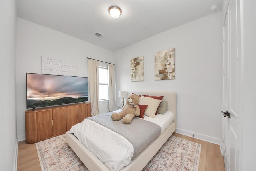 Cozy bedroom with a plush bed, neutral tones, and a large window for natural light, complemented by stylish decor and a modern TV setup.