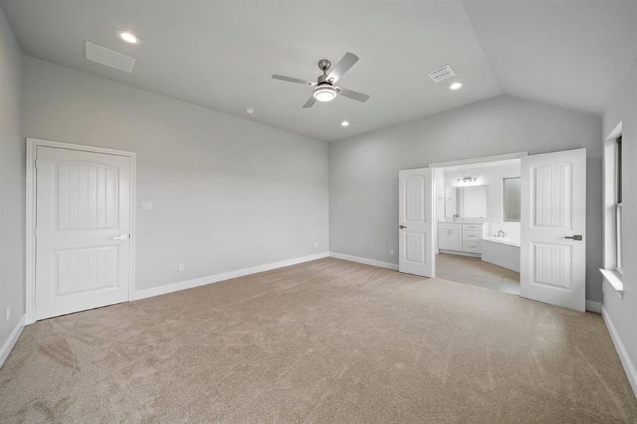 Unfurnished bedroom with lofted ceiling, light colored carpet, ensuite bathroom, and ceiling fan