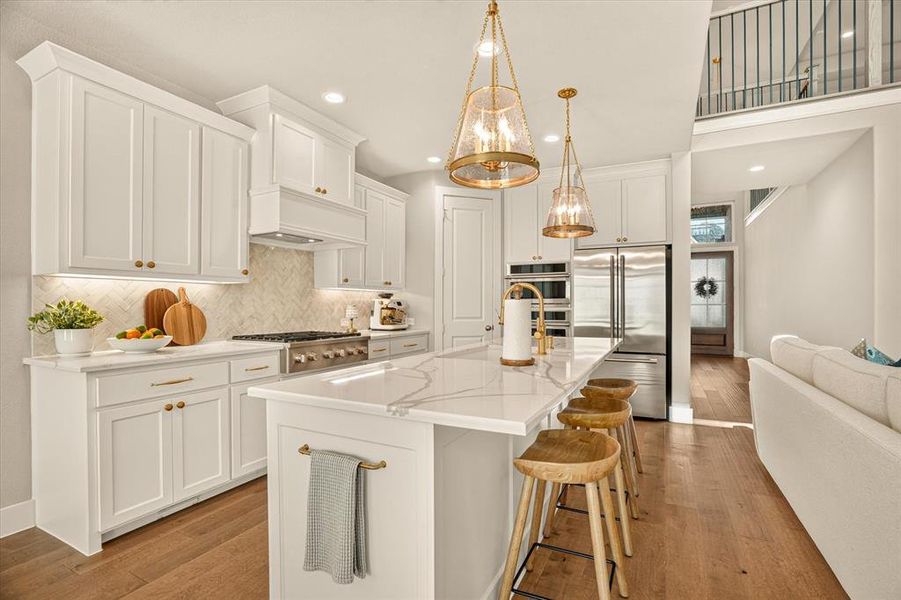 Expansive kitchen featuring a large central island with seating, a high-end range, stainless steel appliances, white cabinetry, and wood-finish flooring Expansive kitchen featuring a large central island with seating, a high-end range, stainless steel appliances, white cabinetry, and wood-finish flooring