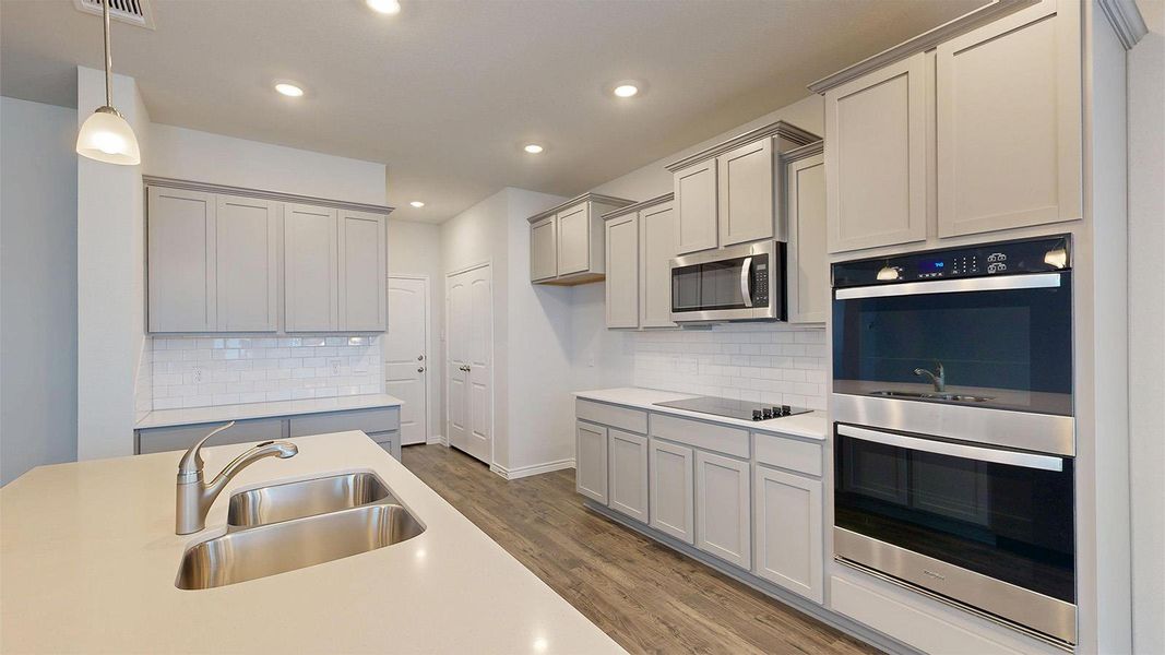 Modern kitchen featuring light gray cabinetry, stainless steel appliances, a subway tile backsplash, and a large island with a double sink